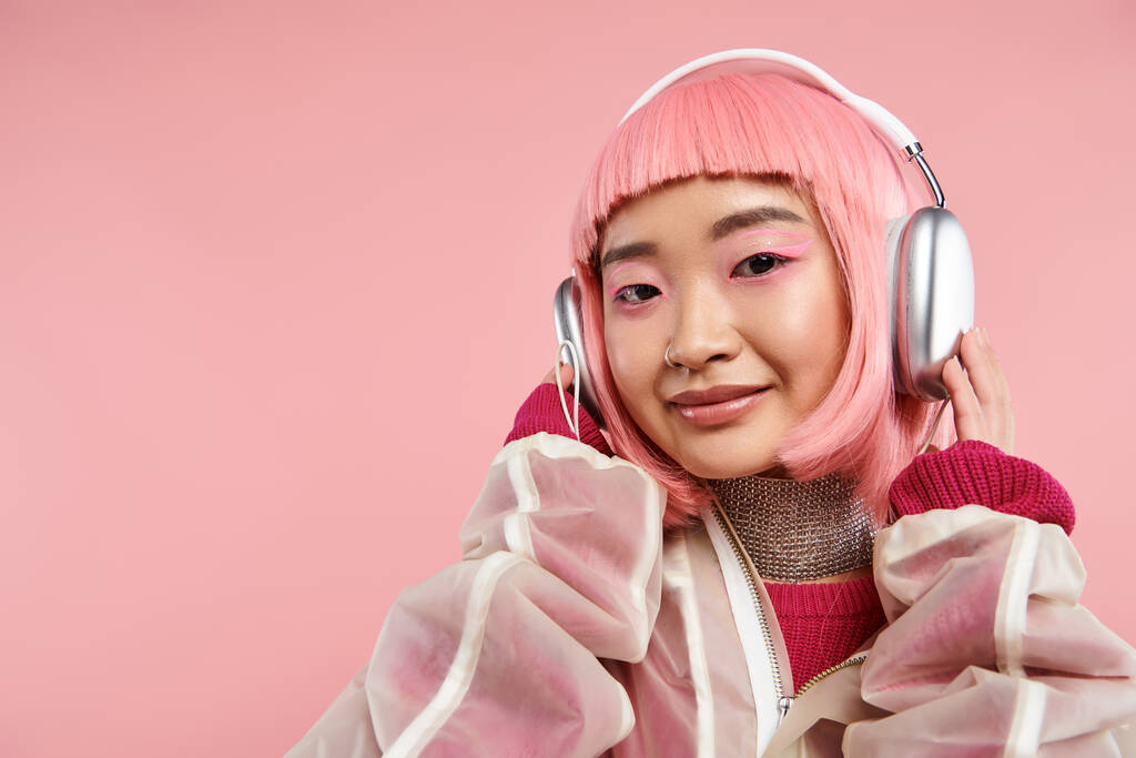 fröhliche asiatische junge Frau mit rosa Haaren posiert mit Kopfhörern vor lebendigem Hintergrund - Foto, Bild