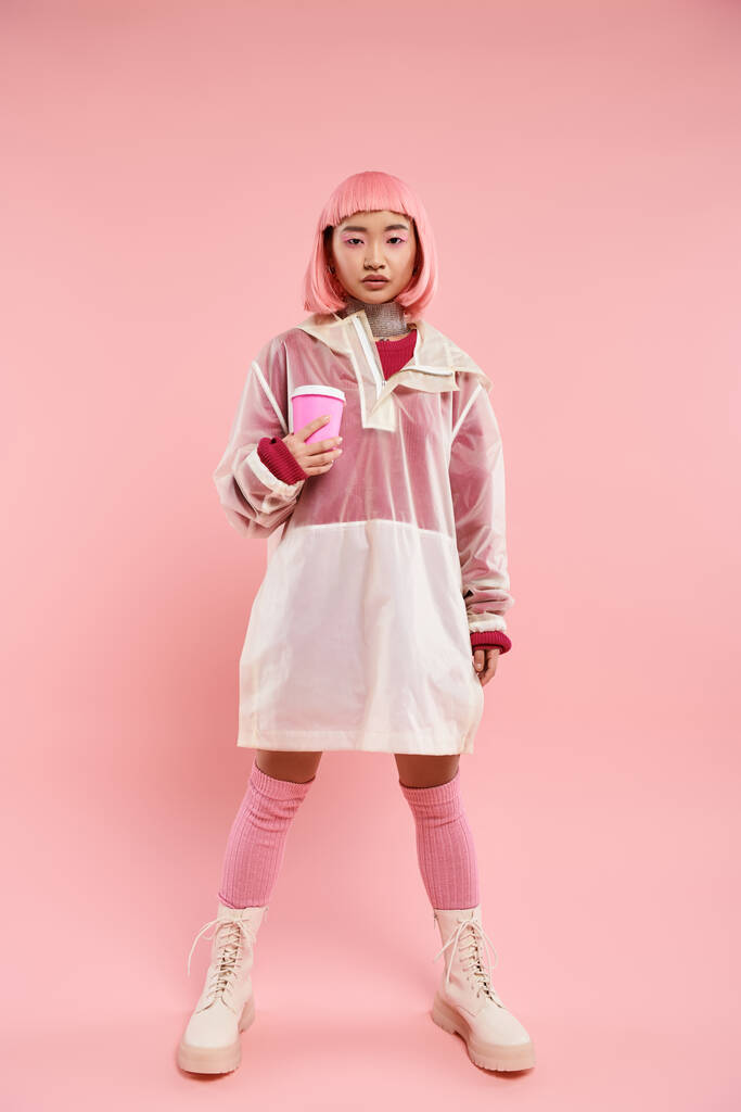 charming asian young woman in pink stylish outfit posing with cup of coffee on vibrant background - Photo, Image
