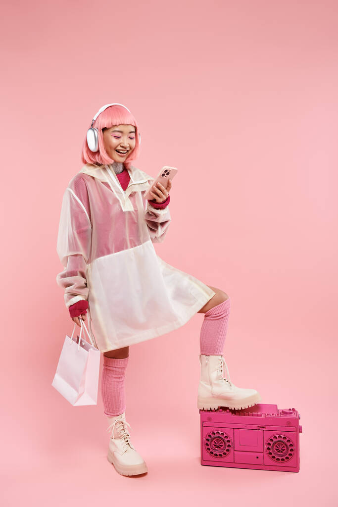 hermosa mujer asiática en auriculares mensajes de texto en el teléfono inteligente y la celebración con paquetes de compras - Foto, Imagen