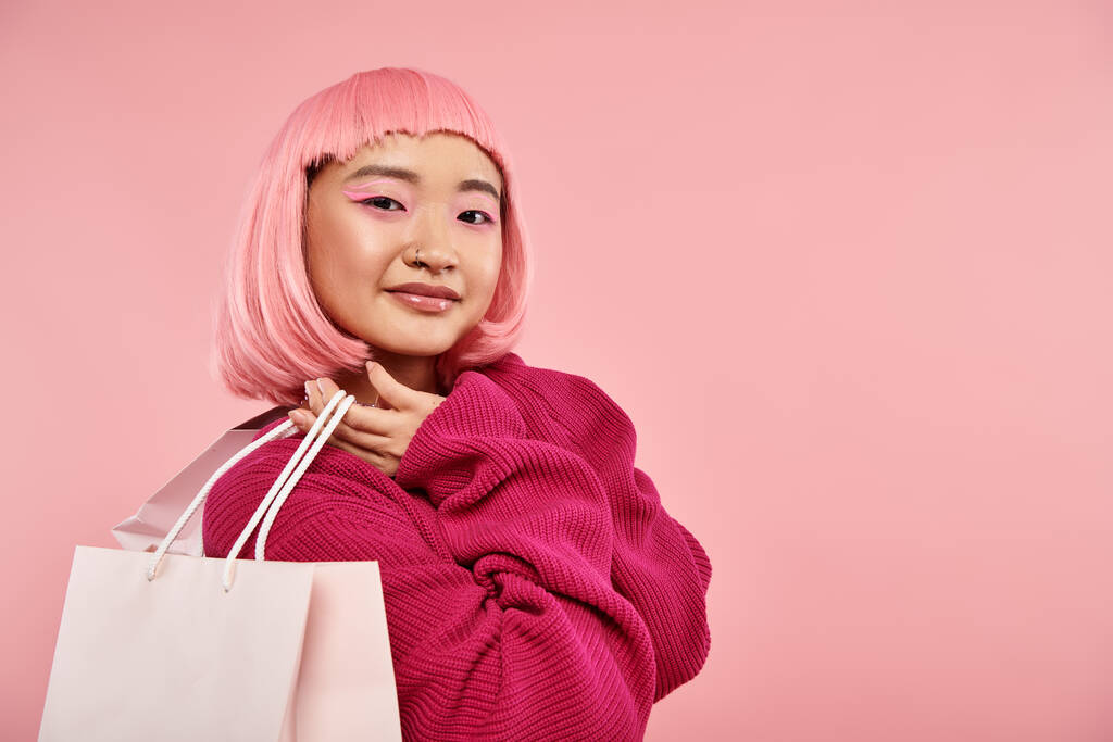 hermosa mujer asiática en 20s con pelo rosa y maquillaje posando con paquetes sobre fondo vibrante - Foto, imagen