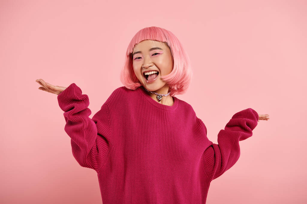 vidám ázsiai fiatal nő nagy pulóverben vállat vonva boldogan rózsaszín háttér - Fotó, kép