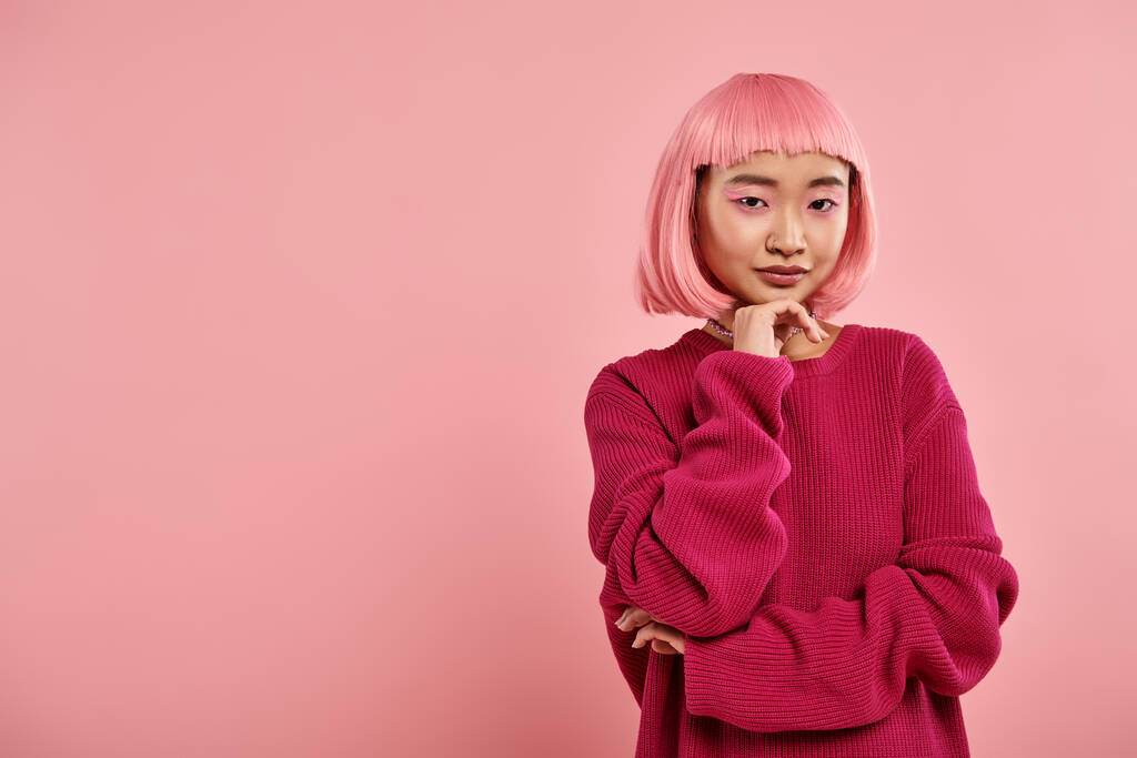 уверенная азиатская девушка с розовыми волосами в большой свитер поддержки подбородок с рукой на ярком фоне - Фото, изображение