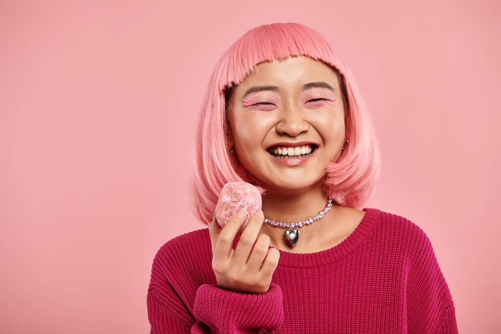 glücklich asiatische junge Frau lächelt und hält Mochi mit der Hand vor rosa Hintergrund - Foto, Bild