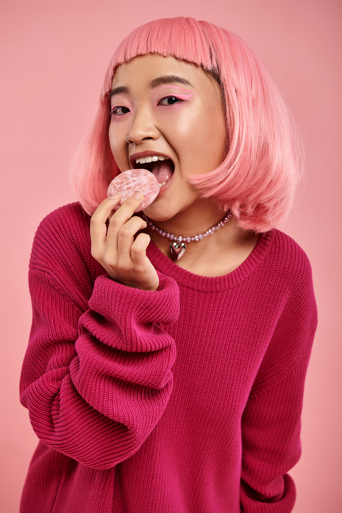 υπέροχο ασιατικό νεαρό κορίτσι με ροζ μαλλιά και μακιγιάζ τρώει mochi σε ζωντανό φόντο - Φωτογραφία, εικόνα