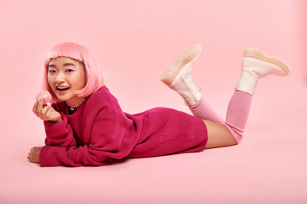 Verspielte Asiatin im pulsierenden Pullover-Outfit mit Mochi vor rosa Hintergrund - Foto, Bild