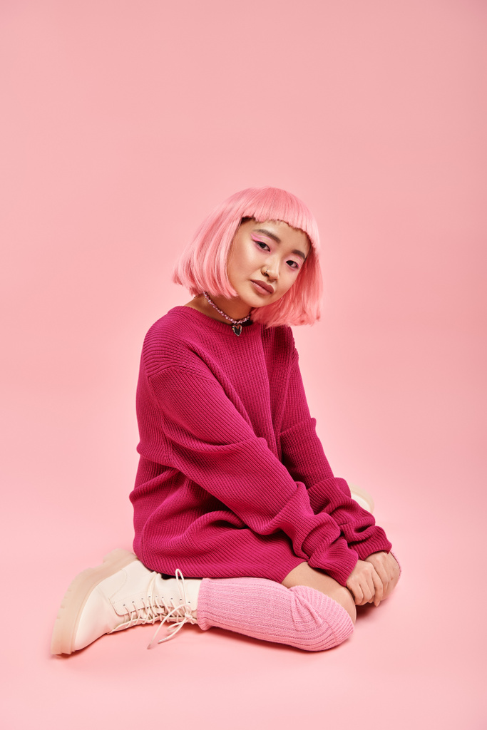 活気に満ちた背景に座っている大きなセーター衣装のピンクの髪の若いアジアの女性 - 写真・画像