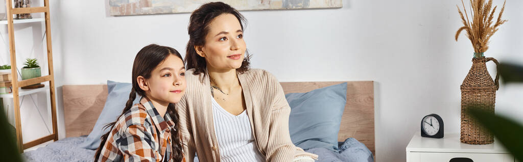 Uma mulher sentada ao lado de uma jovem em uma cama acolhedora, compartilhando momentos sinceros juntos em casa. - Foto, Imagem