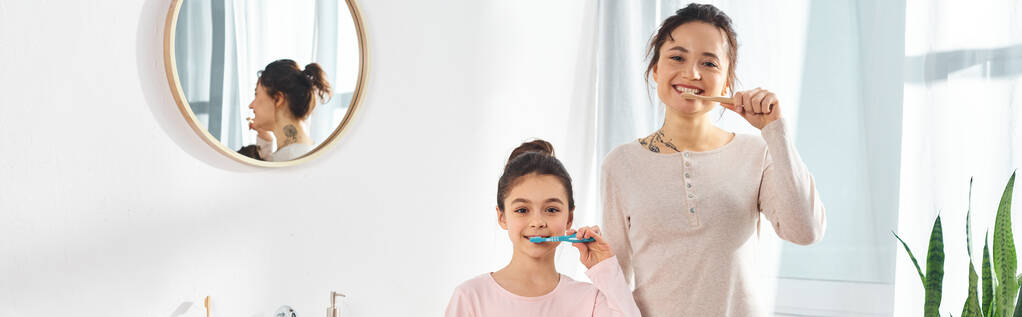 een brunette vrouw en haar tiener dochter bezighouden met hun ochtend routine, poetsen hun tanden in een moderne badkamer. - Foto, afbeelding
