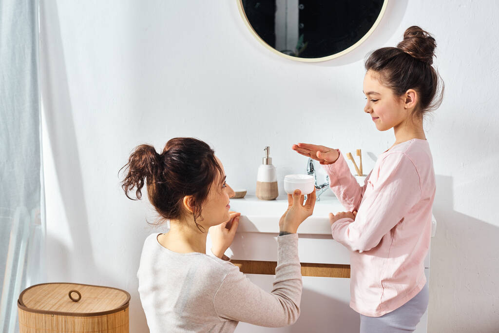 A brunette woman and her preteen daughter are standing together in a modern bathroom, engaged in their beauty and hygiene routine. - Photo, Image
