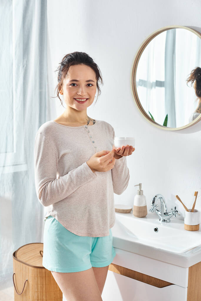 A brunette woman stand in front of a modern bathroom sink, engaging in their beauty and hygiene routine. - Photo, Image