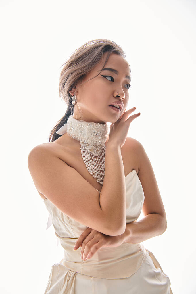 gentil asiático jovem noiva com sofisticação colar moldando com as mãos para rosto no fundo branco - Foto, Imagem