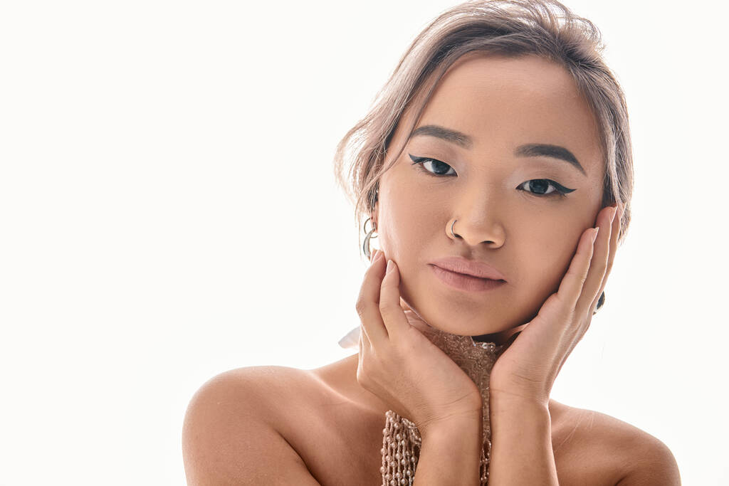 portrét okouzlující asijské dívky s bílým náhrdelníkem objetí na tvář s rukama na světlém pozadí - Fotografie, Obrázek