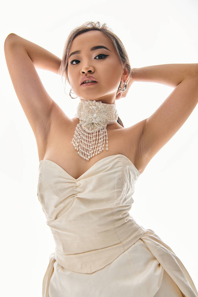 alluring asian young woman in bridal outfit looking to camera and putting hands behind head - Photo, Image