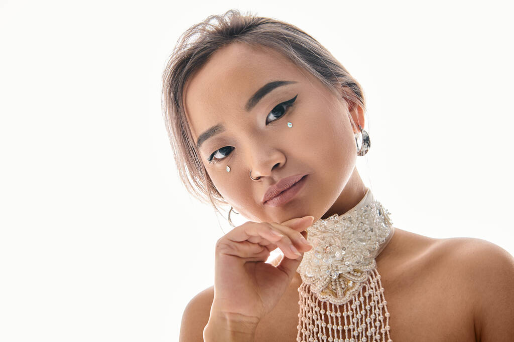 atrakcyjny Azji młoda kobieta z elegancki makijaż pochylenie głowa w bok i patrząc na aparat - Zdjęcie, obraz
