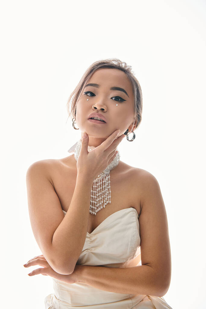 elegante asiático jovem noiva no branco colar delicado tocar para rosto com a mão no luz fundo - Foto, Imagem