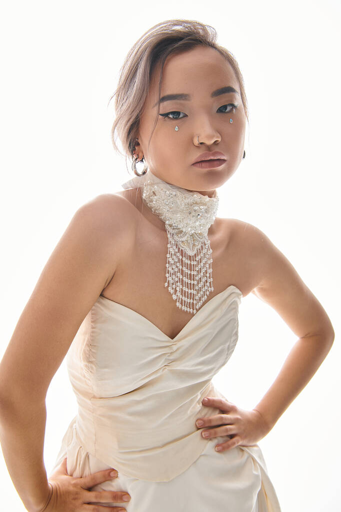 selbstbewusste asiatische junge Braut in eleganter Halskette und Kleid posiert auf weißem Hintergrund - Foto, Bild