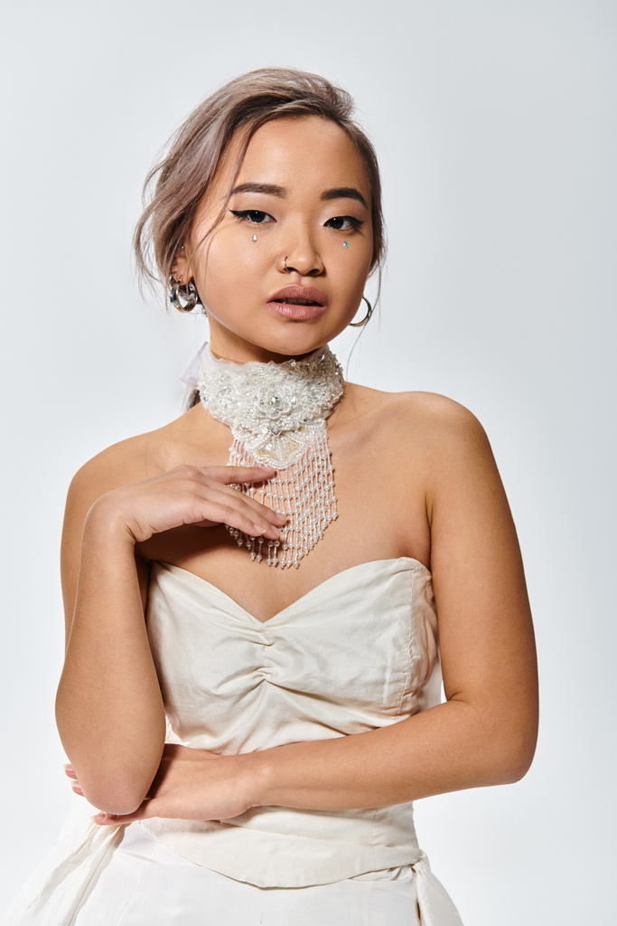 elegante asiatische Braut zarte Berührung zu weißer Halskette und Blick in die Kamera auf hellem Hintergrund - Foto, Bild