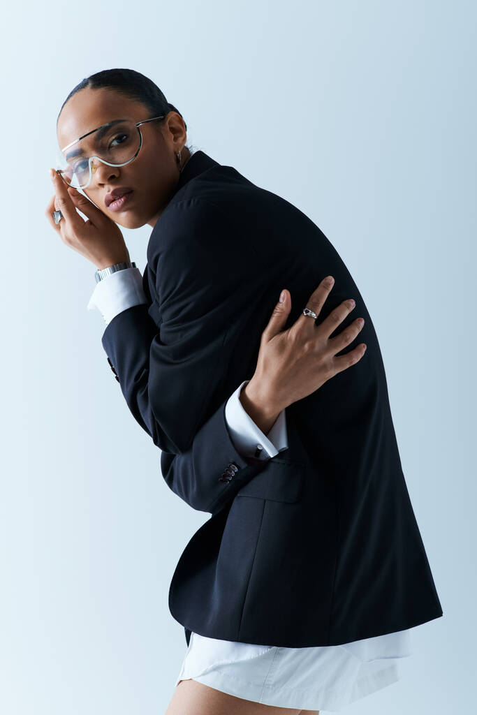 Uma mulher negra elegante em um terno e gravata confiantemente posando em um ambiente de estúdio. - Foto, Imagem