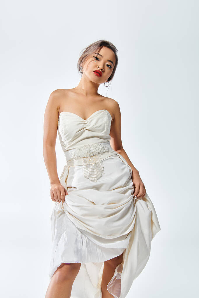 elegante mujer asiática en traje blanco elegante con labios rojos cabeza inclinada y levantó su vestido - Foto, Imagen