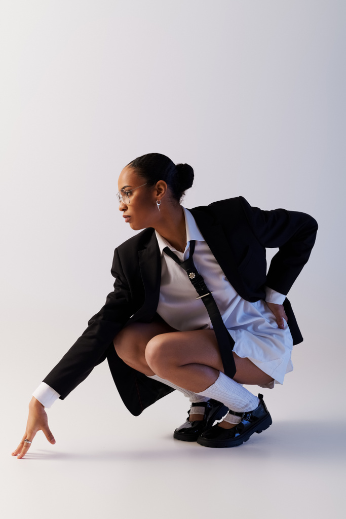 Jeune femme afro-américaine en costume et cravate à genoux dans un cadre de studio - Photo, image