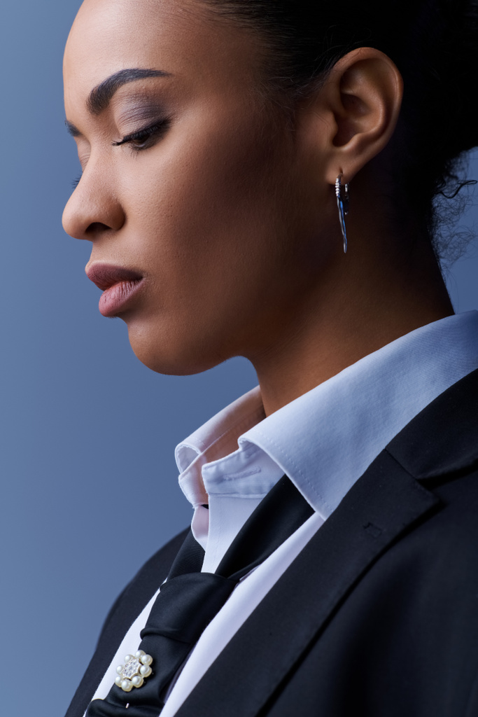 Fiatal afro-amerikai nő öltönyben és fülbevalóban bámul a távolba.. - Fotó, kép