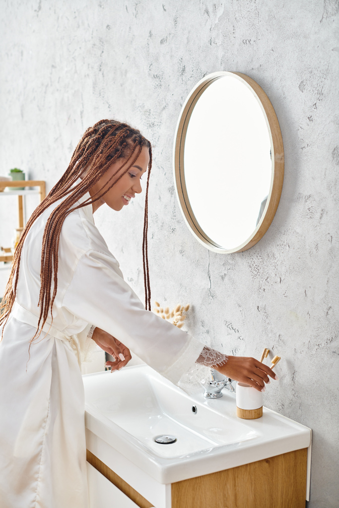 Afrikkalainen amerikkalainen nainen, jolla on afro-punokset, pesee kätensä modernissa kylpyhuoneessa, harjoittelemalla henkilökohtaista hygieniaa ja itsehoitoa.. - Valokuva, kuva
