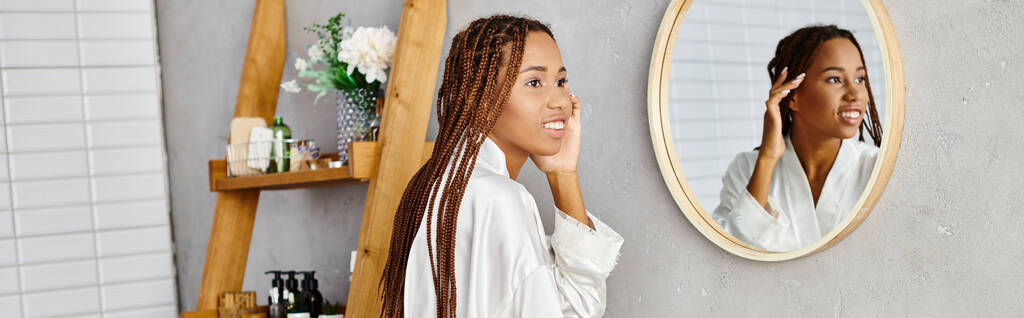 Egy afro-copfos afro-amerikai nő áll a tükör előtt, és a haját fésüli egy modern fürdőszobában.. - Fotó, kép