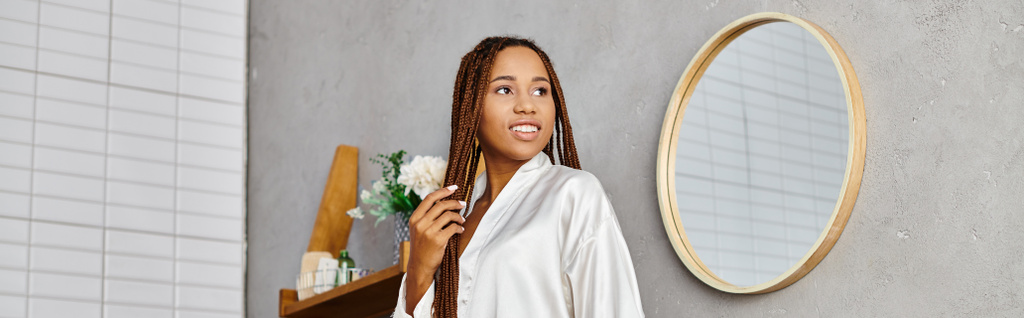 Rasta saçlı Afrikalı Amerikalı bir kadın modern bir banyoda aynanın önünde duruyor ve görünüşüne hayran.. - Fotoğraf, Görsel