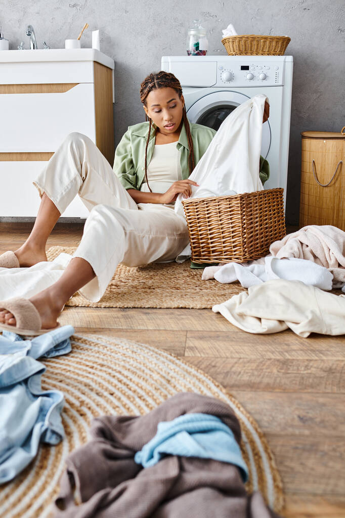 アフリカ系アメリカ人女性 アフリカ系アメリカ人女性が床に座って洗濯物の山の隣に座り,家の振り付けの最中に深く考えました.. - 写真・画像