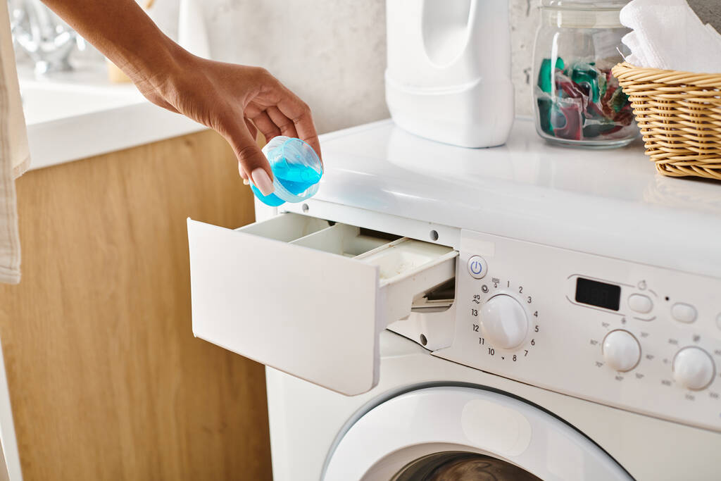 Een Afro-Amerikaanse vrouw houdt een gel capsule pod in de voorkant van een wasmachine, terwijl het doen van de was in een badkamer. - Foto, afbeelding