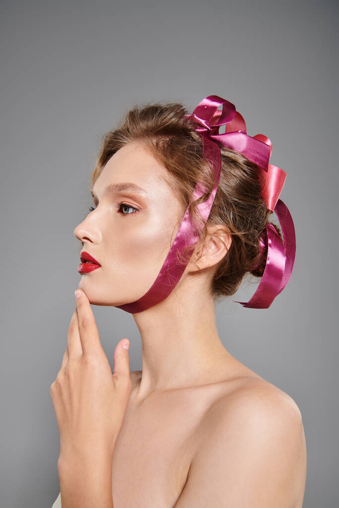 Молода жінка з класичними позуваннями краси в студії, виключаючи елегантність, одягнені в рожевий лук на голові. - Фото, зображення