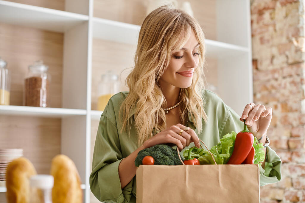 女性は自宅でキッチンで新鮮な野菜の完全な紙袋を保持しています. - 写真・画像