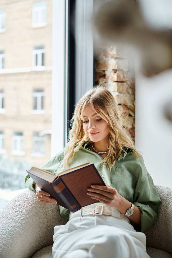 Uma mulher sentada em uma cadeira em casa, absorvida na leitura de um livro. - Foto, Imagem