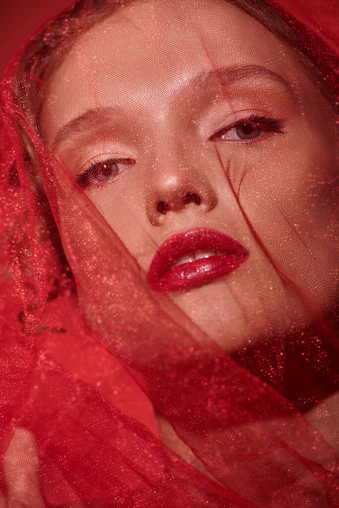 Молодая женщина излучает элегантность в студии, украшенная ярко-красной вуалью и ярко-красной помадой. - Фото, изображение