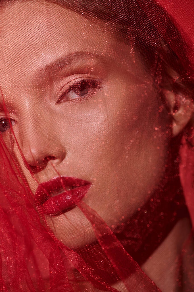 Een jonge vrouw met levendig rood haar en bijpassende lippenstift straalt tijdloze elegantie uit in een studio tegen een zwarte achtergrond. - Foto, afbeelding