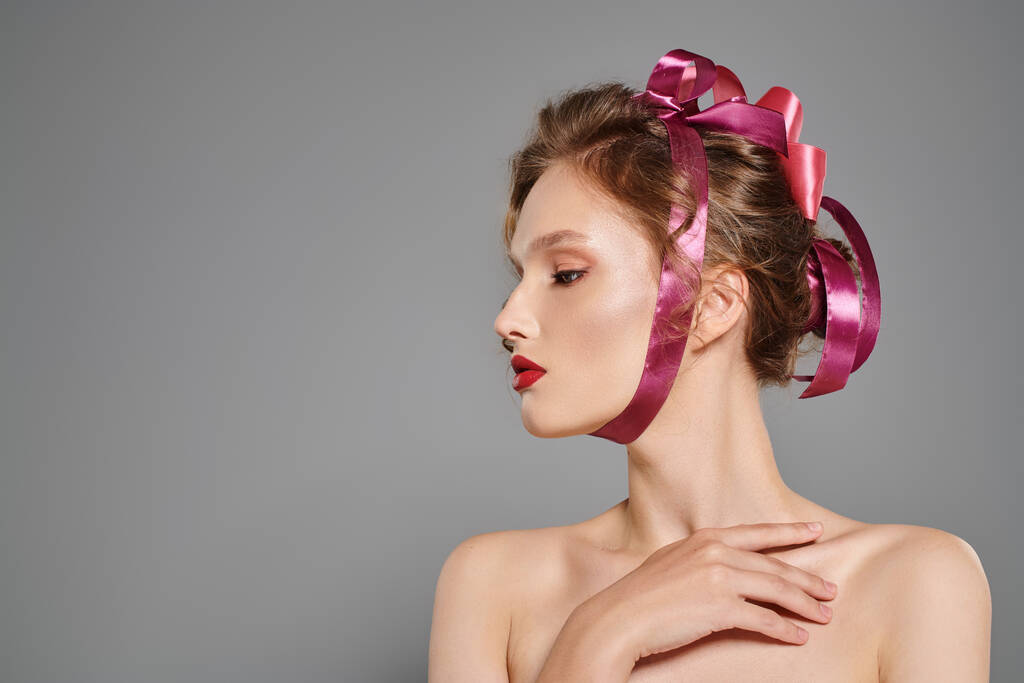 Młoda kobieta z klasyczną urodą pozuje w studio, jej włosy ozdobione delikatną różową wstążką. - Zdjęcie, obraz
