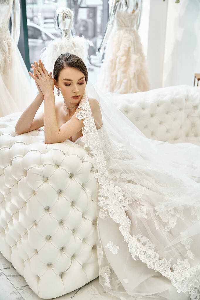 Молодая брюнетка невеста в потрясающем свадебном платье мирно отдыхает на роскошной кровати в свадебном салоне. - Фото, изображение