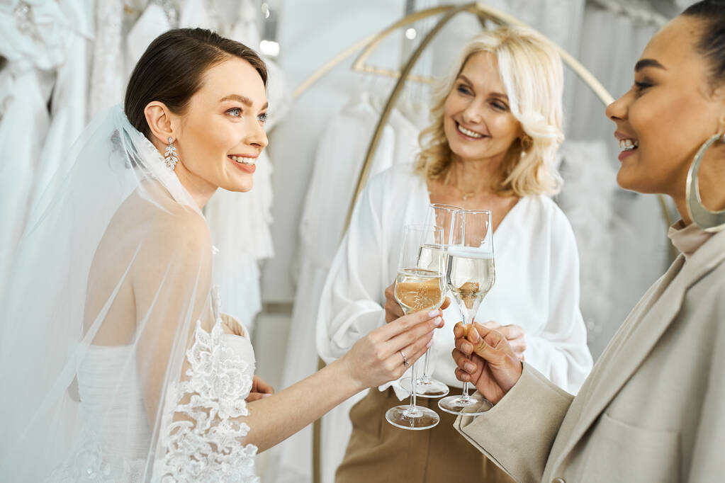una giovane sposa in abito da sposa e sua madre di mezza età, che regge bicchieri di vino e sorride gioiosamente. - Foto, immagini