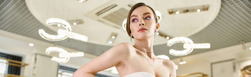 A stunning brunette bride in a chic white dress stands poised in a glamorous wedding salon. - Photo, Image