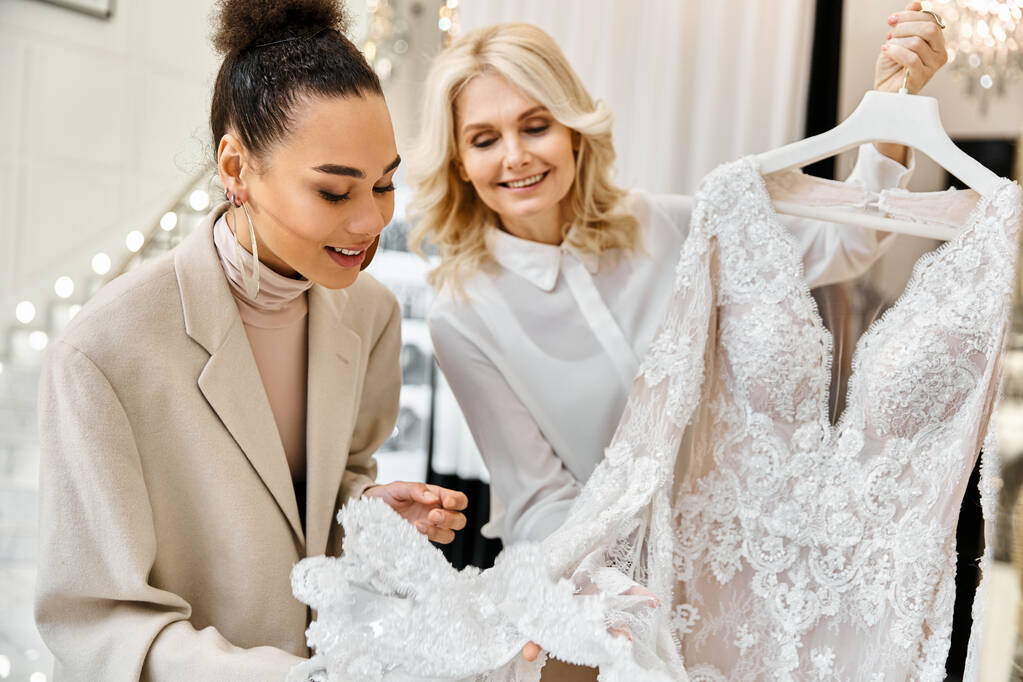 Дві жінки захоплюються білим платтям на вішалці у весільному магазині. Помічник нареченої і магазину обговорюють сукню. - Фото, зображення