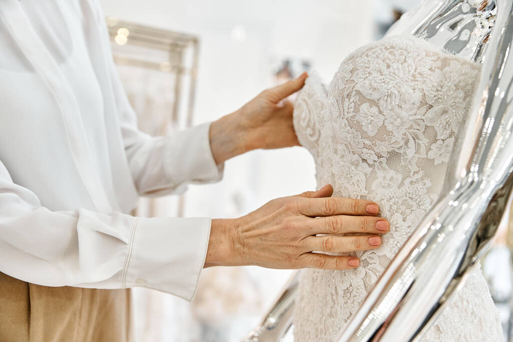 Egy középkorú bevásárló asszisztens magabiztosan áll egy rakás elegáns ruha előtt egy esküvői szalonban.. - Fotó, kép