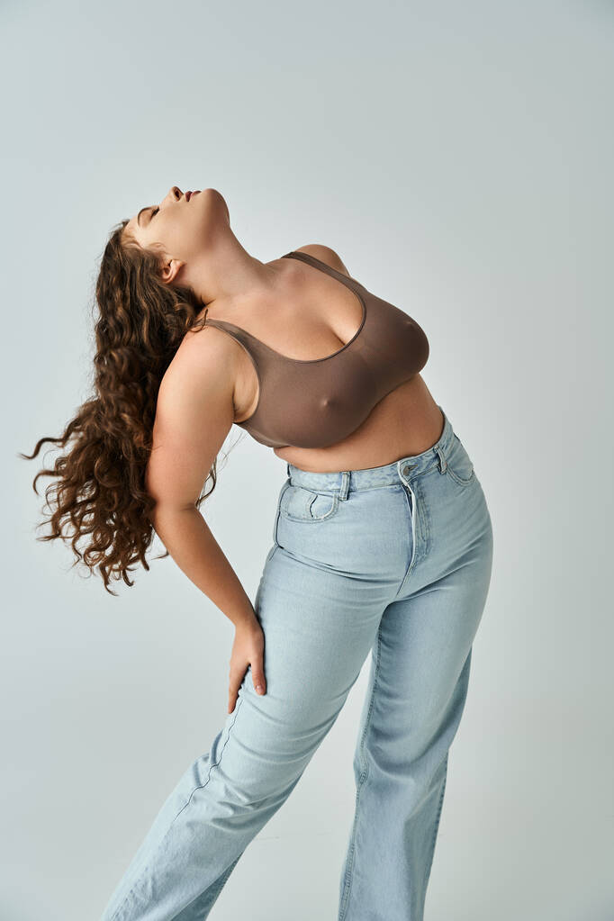 alluring plus size woman in brown bra and blue jeans with curly hair putting head to behind - Photo, Image