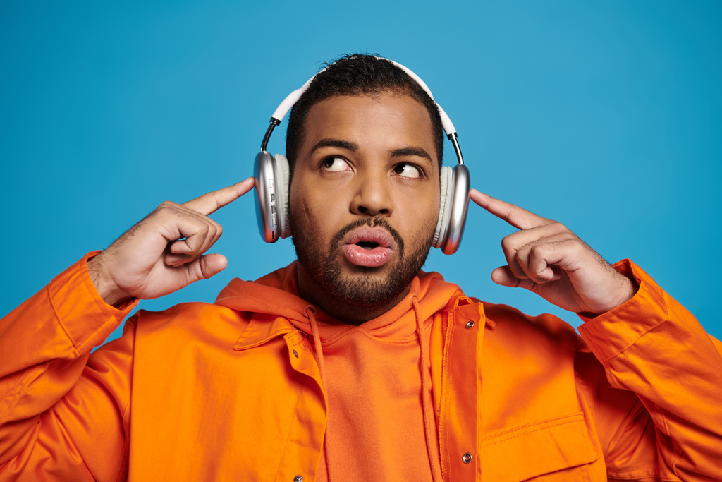 attractive african american young man looking to up and touching fingers to headphones on head - Photo, Image