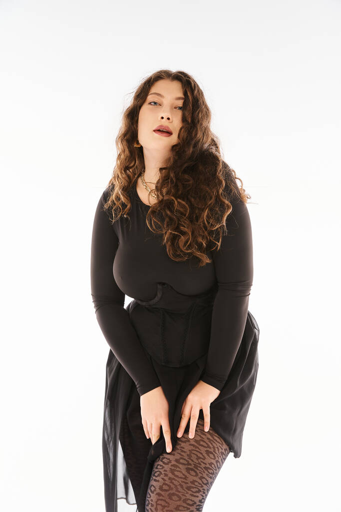 mulher curvilínea atraente em roupa elegante preto com cabelo encaracolado posando com as mãos na coxa - Foto, Imagem