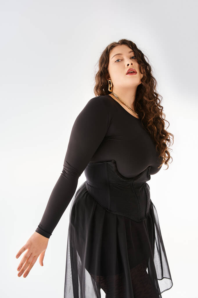seductora mujer de talla grande en traje elegante negro con pelo rizado posando sobre fondo claro - Foto, imagen
