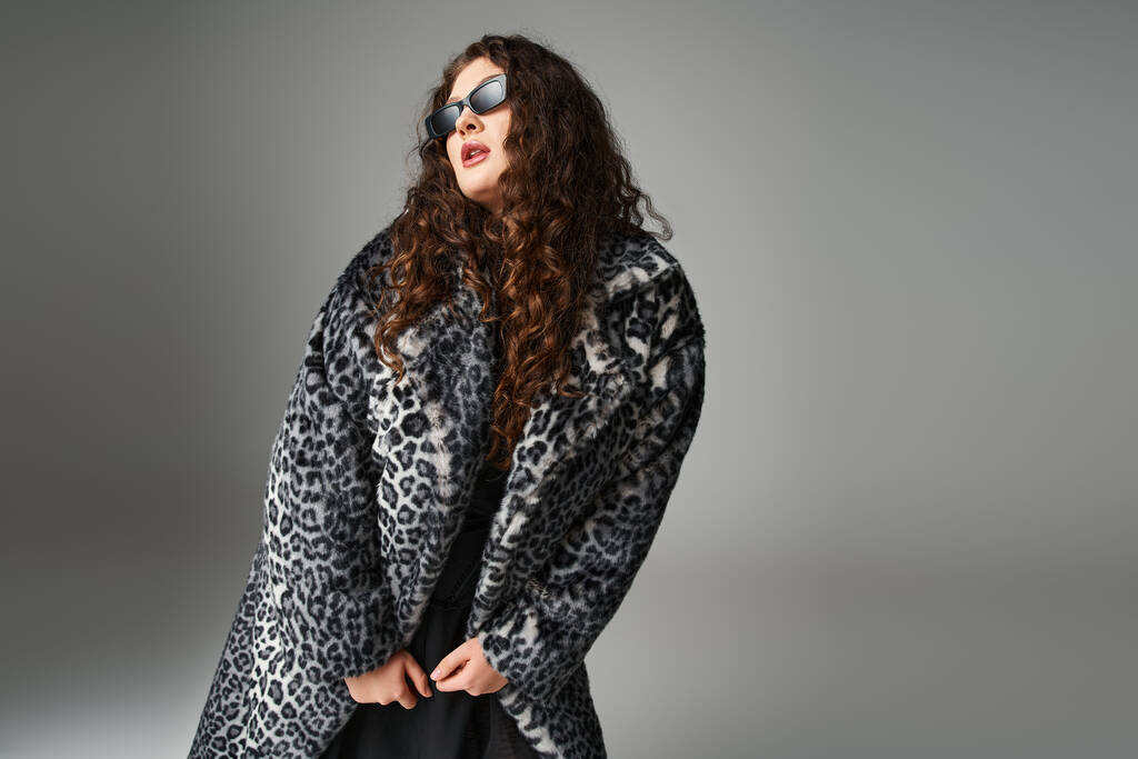 sedutor mulher plus size em casaco de pele de leopardo e óculos de sol inclinados para a frente e olhando para o lado - Foto, Imagem