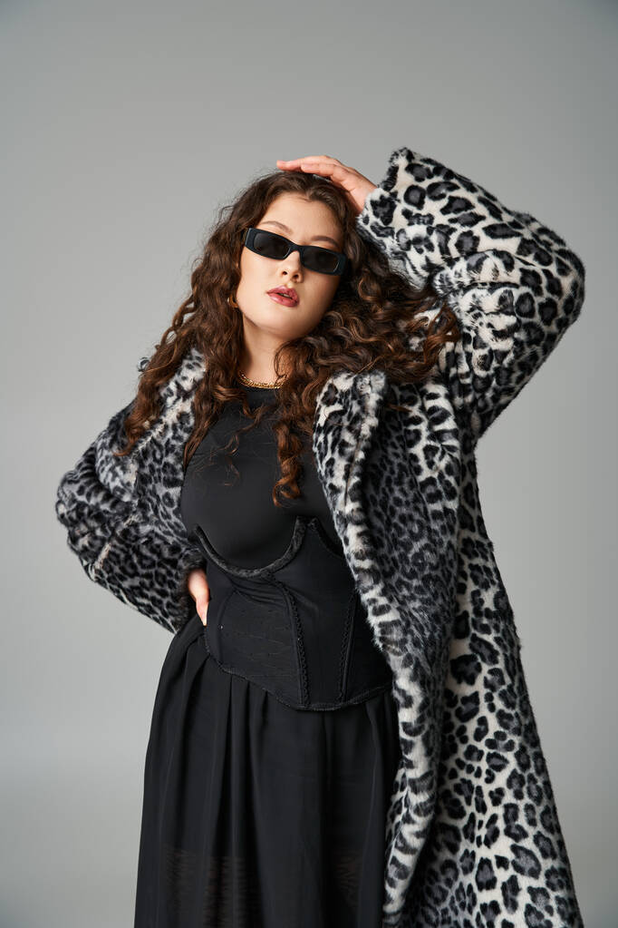 attraente giovane donna curvy in pelliccia di leopardo e occhiali da sole con le mani sulla vita e la testa - Foto, immagini