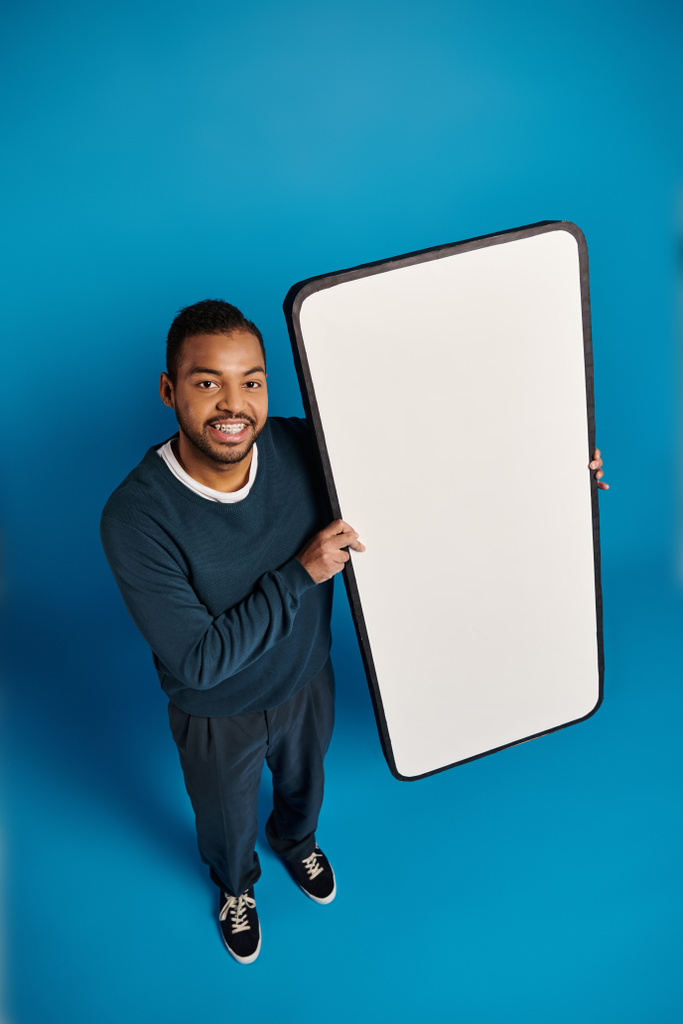 top shot di giovane afroamericano con banner bianco o smartphone in mano contro il blu - Foto, immagini