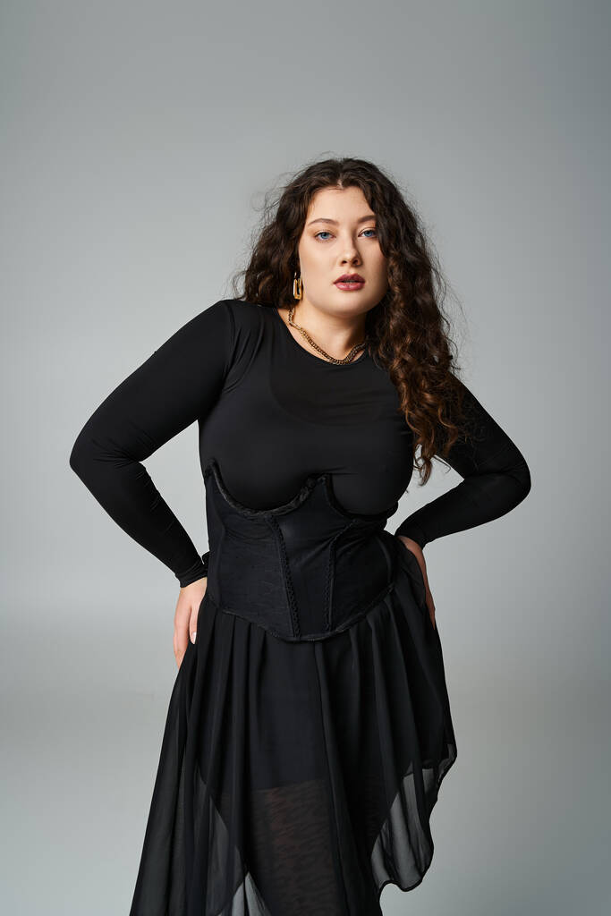 beautiful plus size young girl in black outfit  posing with hands on hips on grey background - Photo, Image