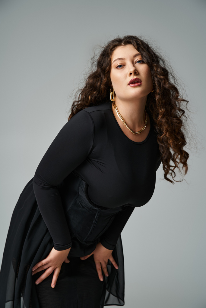 beautiful curvy young woman in black outfit leaning to forward against grey background - Photo, Image